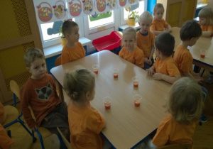 Dzieci siedzące przy stolikach z kubeczkami soku.